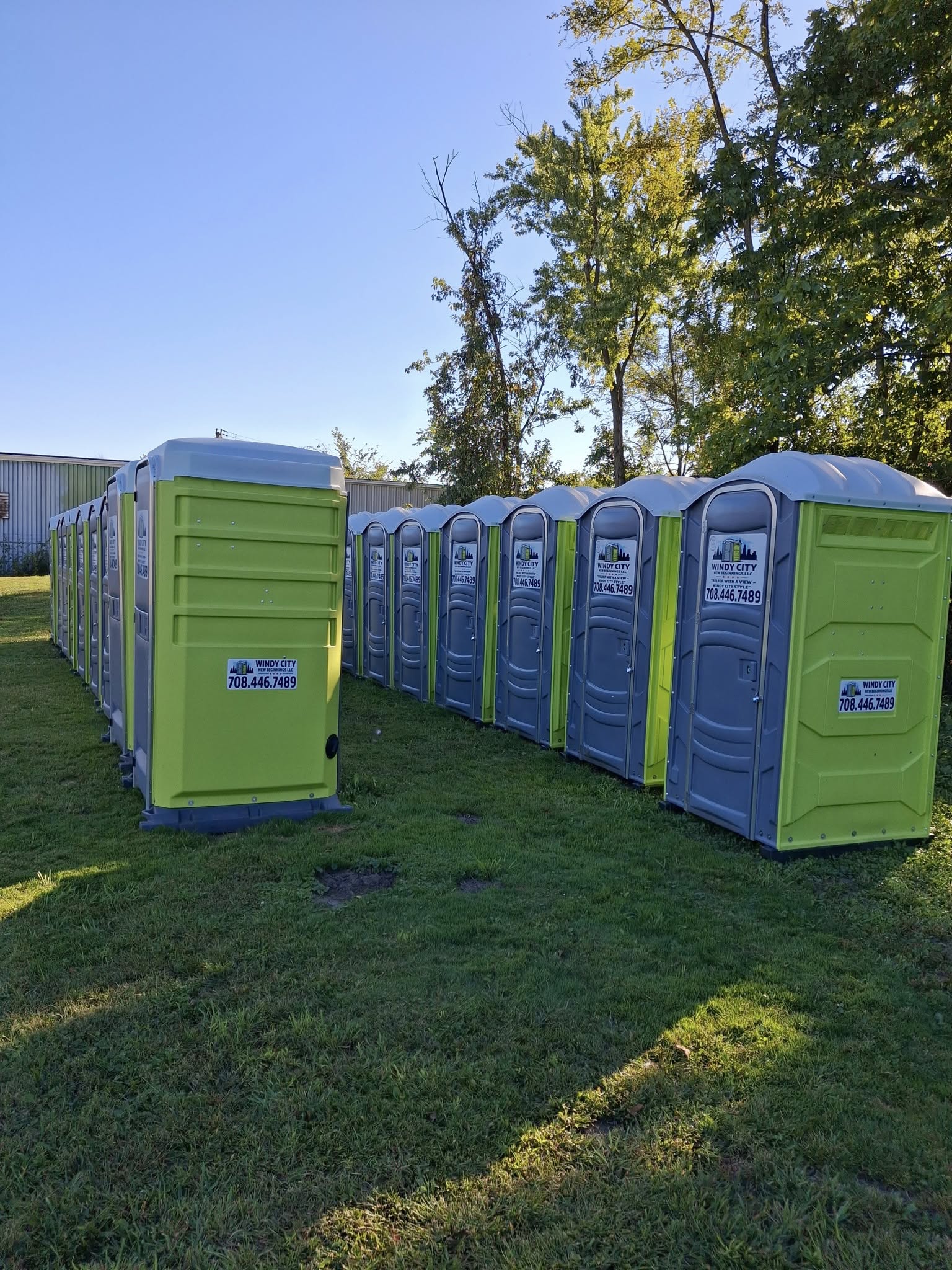 Row of bright lime-green Windy City porta potty units ready for delivery